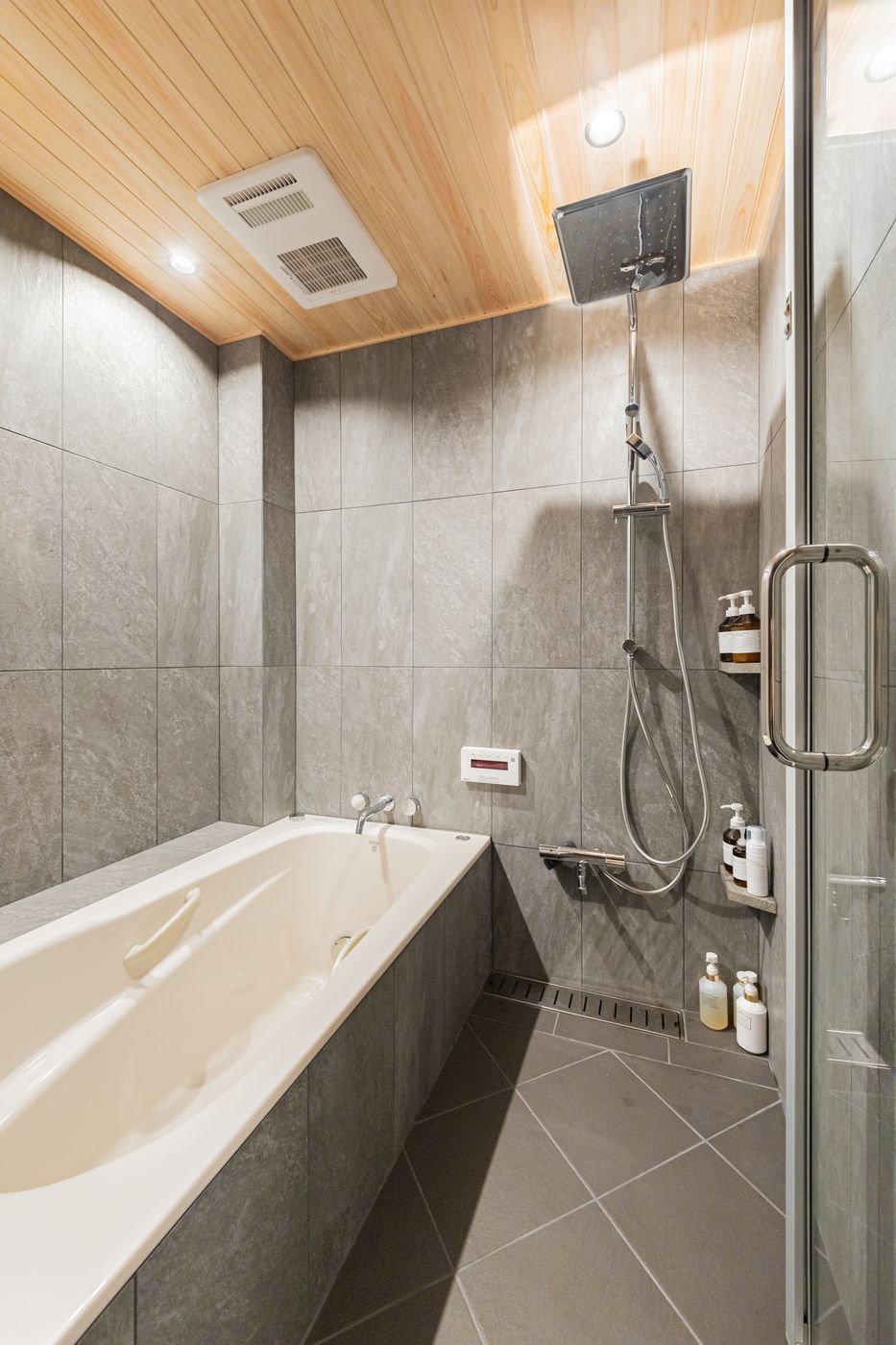 The bathroom of Rin: a deep bathtub and shower under a wooden ceiling, with grey tiles