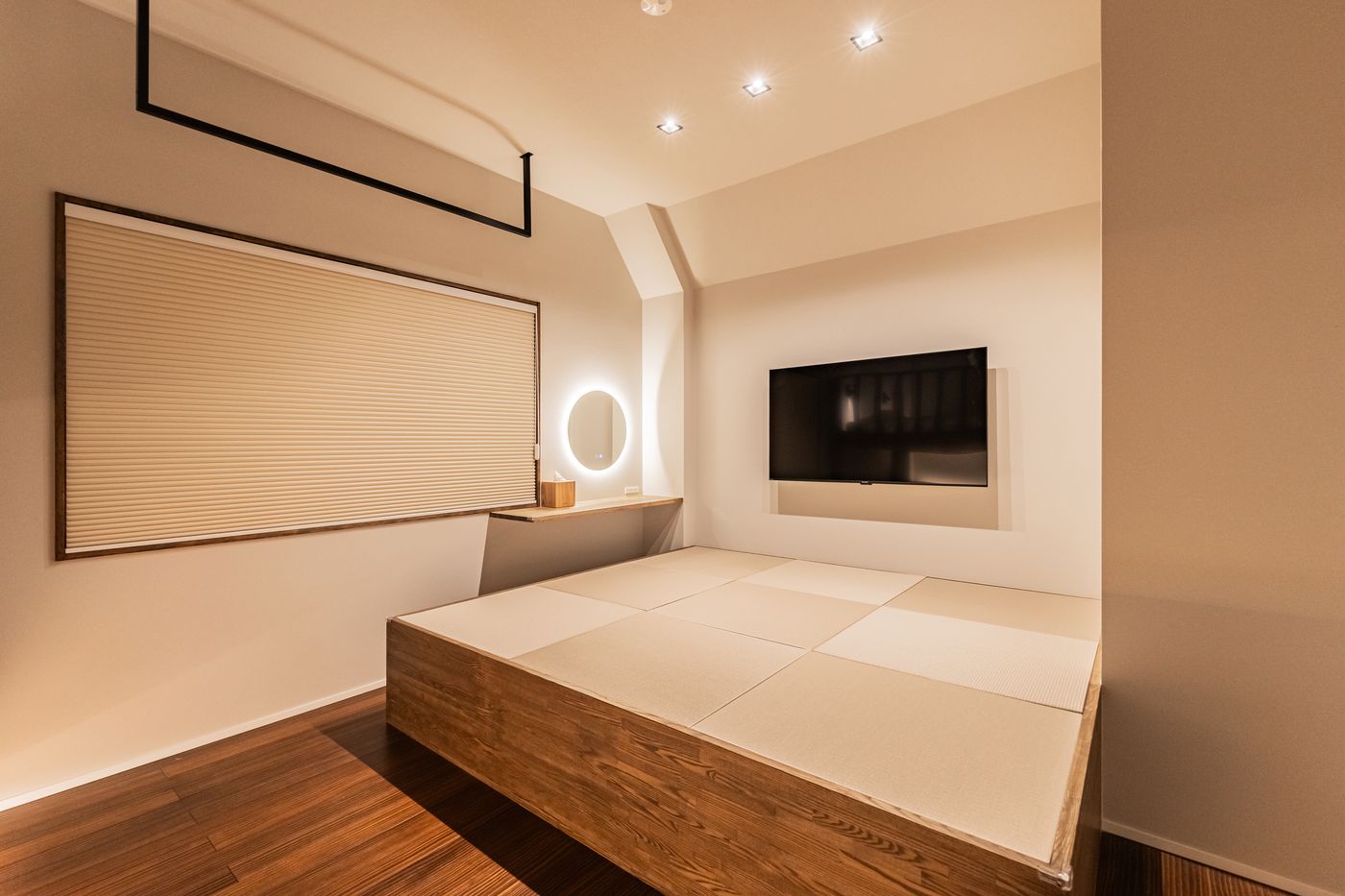 Bedroom one: a low wooden platform bed with tatami, a round mirror and a wall-mounted television